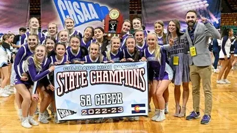 A male and female Glass Doctor owner standing with a group of female cheerleaders holding a banner.