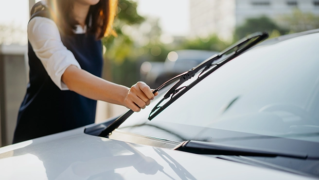 A picture of a person lifting a windshield wiper off a windshield.