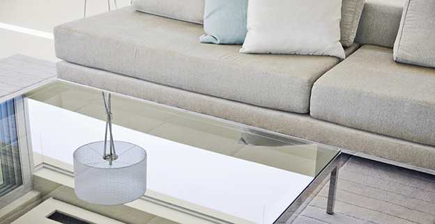 A picture of a custom glass tabletop next to a gray sofa.