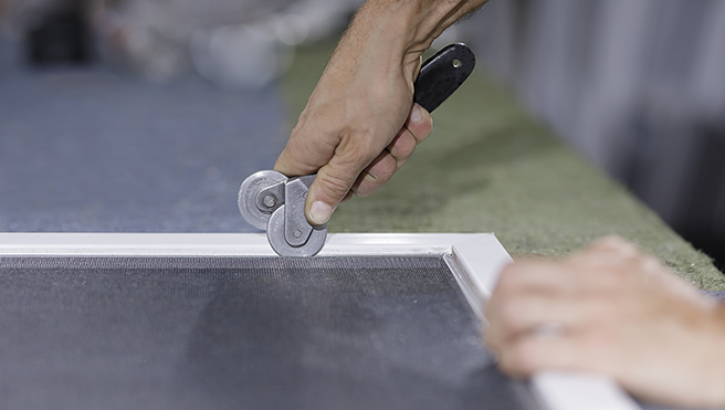 A picture of a pair of hands cutting a window screen.