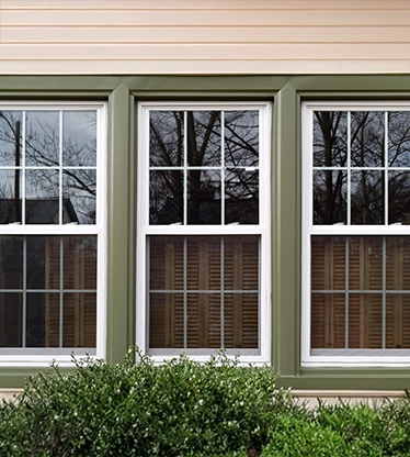 Three new replacement windows with green trim on front of house.