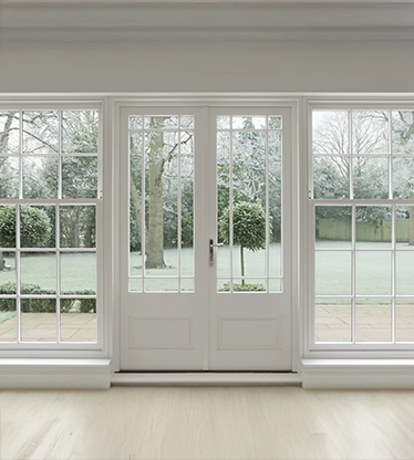 Beautifully crafted Georgian white wooden windows and patio doors with a view towards a wintery garden covered in frost.