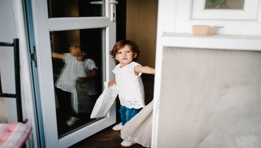 Small child standing next to an open glass door.