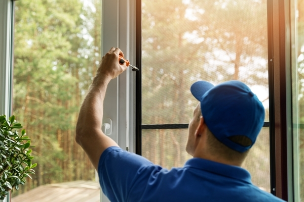 Man wearing a blue shirt installing a window screen in a residential home.