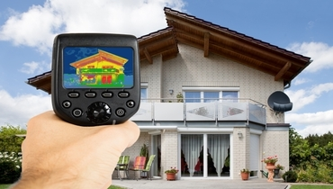 Close-up of person holding a handheld infrared thermal camera outside of a residential home.